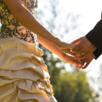 Bride and groom holding hands during their vows at an outdoor wedding ceremony.