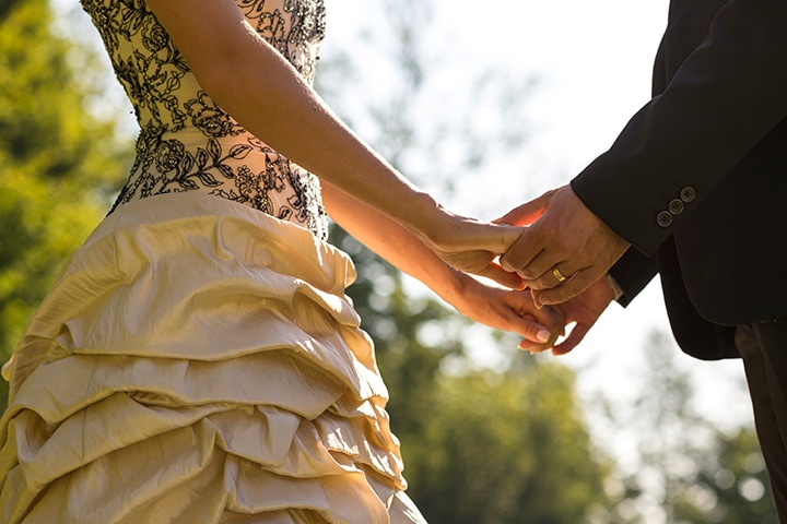 Bride and groom holding hands during their vows at an outdoor wedding ceremony.