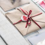 An assortment of natural wedding invitations in envelopes on a white wood table.