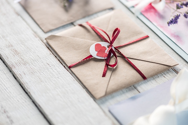 An assortment of natural wedding invitations in envelopes on a white wood table.