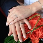 Bride and groom wearing platinum wedding bands displayed over the bride's bouquet.