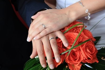 Bride and groom wearing platinum wedding bands displayed over the bride's bouquet.