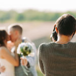 Wedding photographer captures the bride and groom kissing at a sun-filled outdoor wedding.