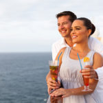 A happy couple celebrates with cocktails on the upper deck of a cruise ship.