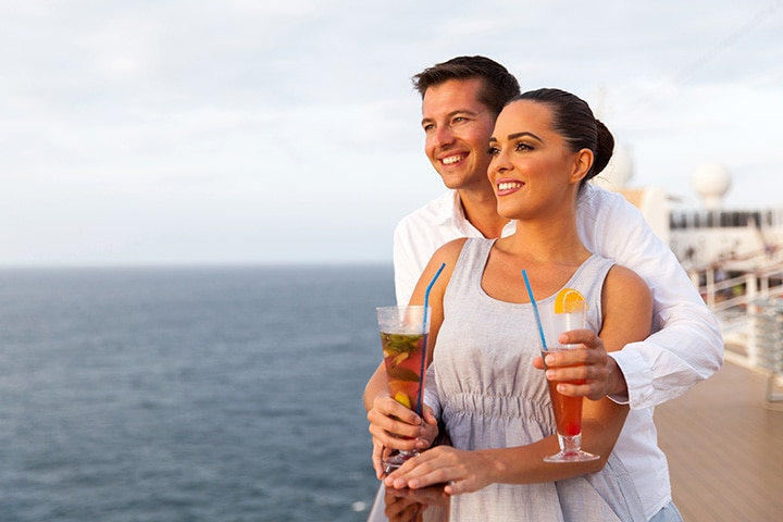 A happy couple celebrates with cocktails on the upper deck of a cruise ship.