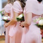 Bridemaids in soft pink dresses holding white rose bouquets.