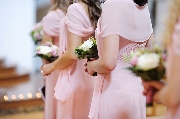 Bridemaids in soft pink dresses holding white rose bouquets.