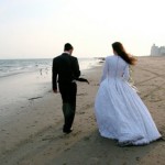 Newly married couple walks along the shoreline on a cool day.