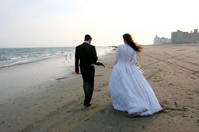 Newly married couple walks along the shoreline on a cool day.