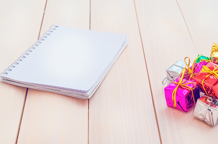 Wedding planning journal on a light wood tabletop with festive wrapped gift favors.