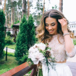 Happy bride with bouquet in a wooded outdoor setting.