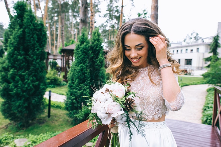 Happy bride with bouquet in a wooded outdoor setting.