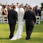 Bride approaches her adoring guests at an outdoor wedding ceremony.