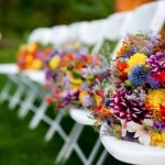 Colorful wildflower bouquets line the bridesmaids' chairs at an outdoor wedding ceremony.