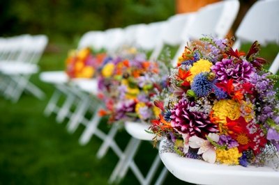 Colorful wildflower bouquets line the bridesmaids' chairs at an outdoor wedding ceremony.