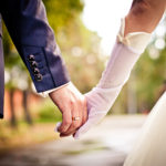 Bride and groom walking hand in hand outdoors.