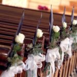 Church pews lined with white roses and festive bows.