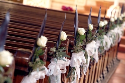 Church pews lined with white roses and festive bows.