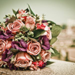 A beautiful antique rose and plum bridal bouquet photographed atop a stone ledge.