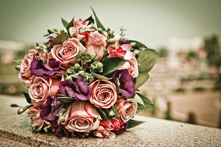 A beautiful antique rose and plum bridal bouquet photographed atop a stone ledge.